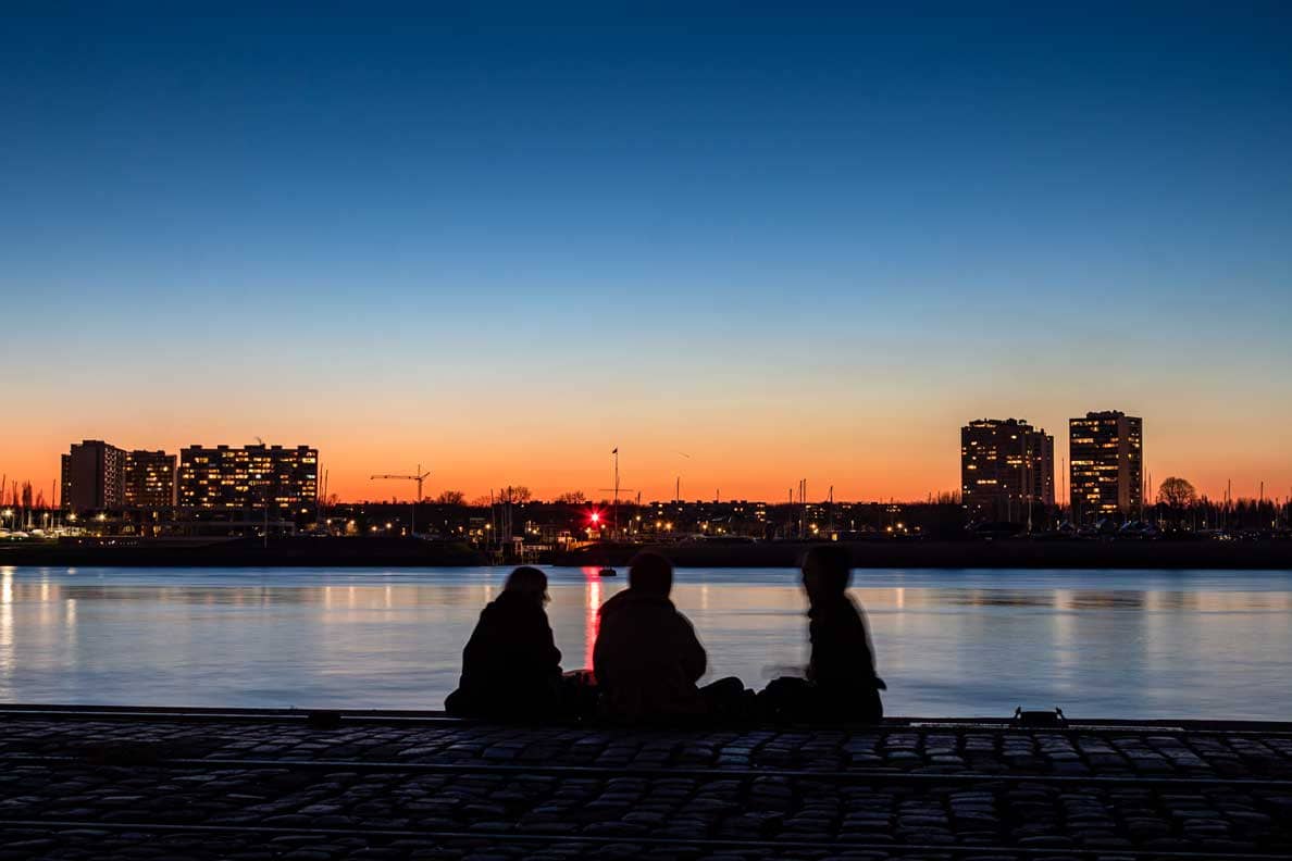 Silhouetten genieten van de zonsondergang aan de Scheldekaaien in Antwerpen