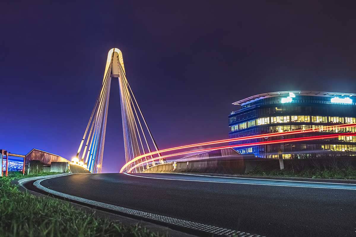 Lighttrail van voorbijrijdende auto aan Ottergembrug met verlicht gebouw op achtergrond