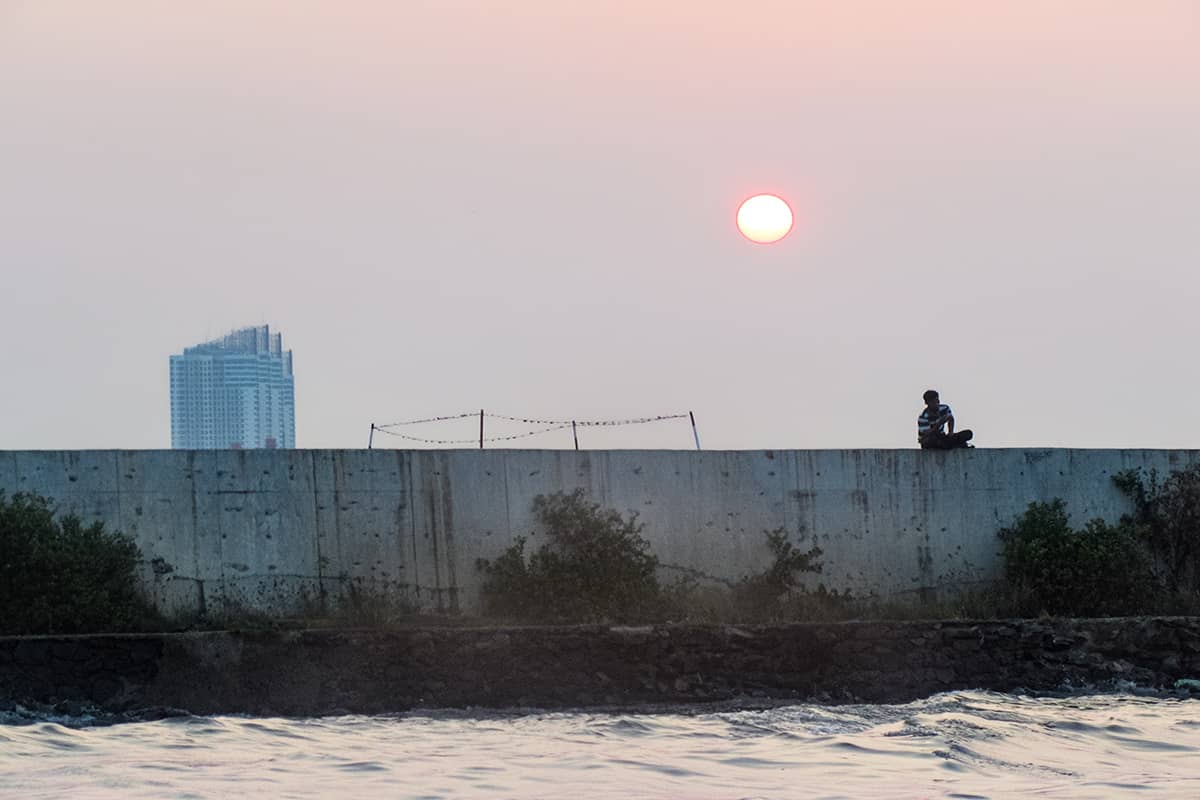 Jongen op muur bij zonsondergang in de oude haven in Jakarta, Indonesië